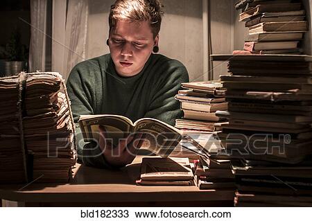 Stock Image - Caucasian man reading stack of books. Fotosearch