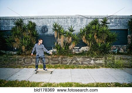Stock Photo - Caucasian man riding skateboard on sidewalk. Fotosearch