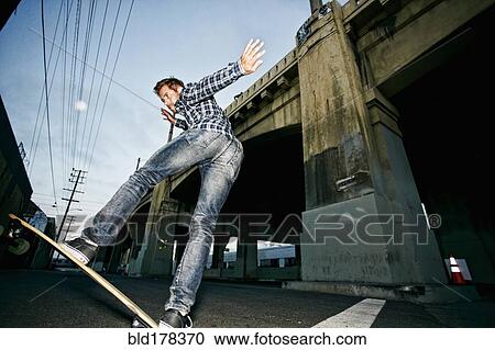Stock Image - Caucasian man riding skateboard outdoors. Fotosearch