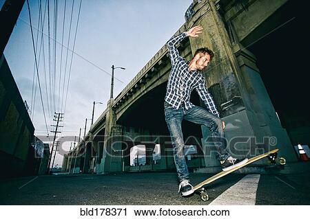 Stock Image - Caucasian man riding skateboard outdoors. Fotosearch