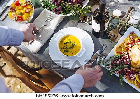 Stock Photograph - Caucasian man setting platter of soup on outdoor table. Fotosearch