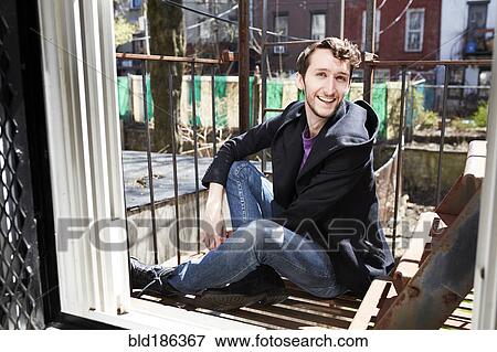 Stock Photo - Caucasian man sitting on fire escape. Fotosearch