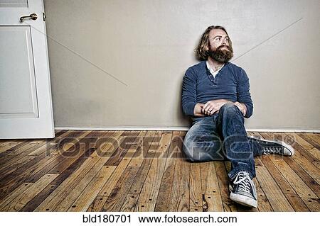 Stock Image - Caucasian man sitting on floor. Fotosearch