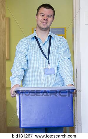 Stock Photo - Caucasian man with Down Syndrome carrying bin in office. Fotosearch