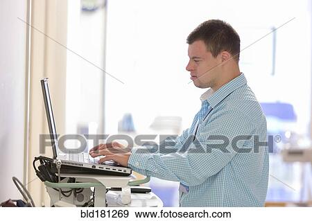 Stock Photo - Caucasian man with Down Syndrome working on laptop in hospital. Fotosearch