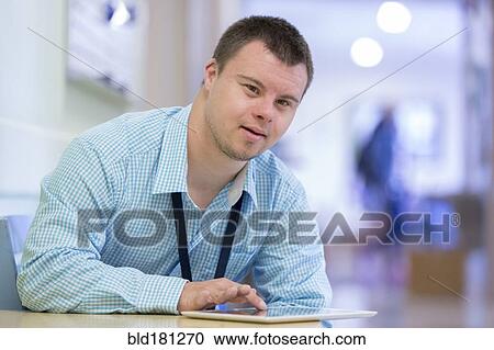 Stock Image - Caucasian man with Down Syndrome using digital tablet in hospital. Fotosearch