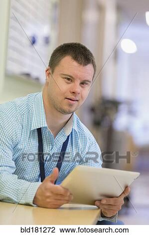 Stock Image - Caucasian man with Down Syndrome using digital tablet in hospital. Fotosearch