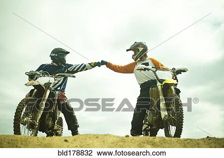 Stock Image - Caucasian men bumping fists on dirt bikes. Fotosearch