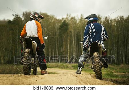 Stock Image - Caucasian men riding dirt bikes on road. Fotosearch