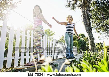 Stock Image - Caucasian mother and daughter riding skateboards on sidewalk. Fotosearch