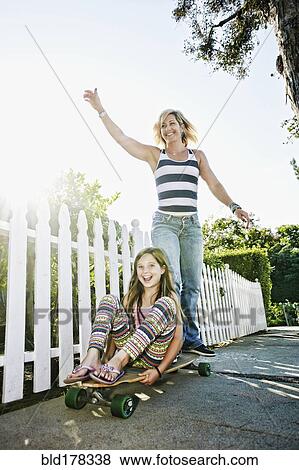 Stock Photo - Caucasian mother and daughter riding skateboard on sidewalk. Fotosearch