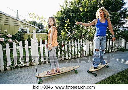 Stock Photography - Caucasian mother and daughter riding skateboards on sidewalk. Fotosearch