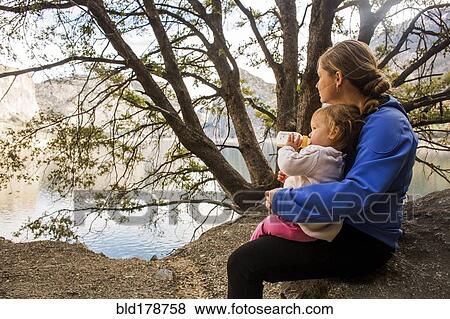 Stock Photo - Caucasian mother and daughter sitting at lake. Fotosearch
