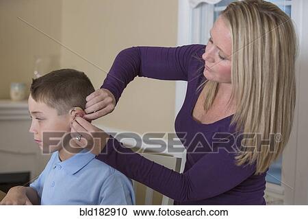 Stock Image - Caucasian mother fitting deaf son with hearing aid. Fotosearch