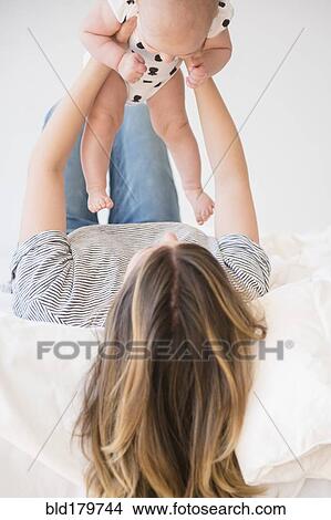 Picture - Caucasian mother holding baby daughter on bed. Fotosearch