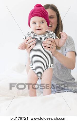 Stock Image - Caucasian mother holding baby daughter on bed. Fotosearch