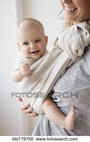 Stock Image - Caucasian mother holding baby daughter in sling. Fotosearch
