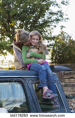Stock Image - Caucasian mother hugging daughter on roof of truck. Fotosearch