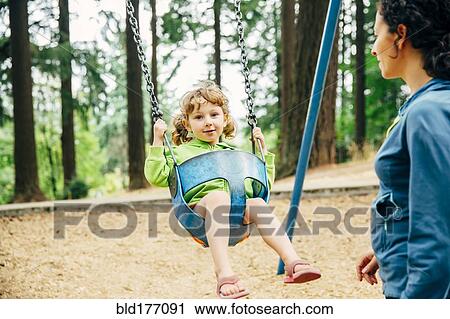 Stock Image - Caucasian mother pushing daughter on swing. Fotosearch