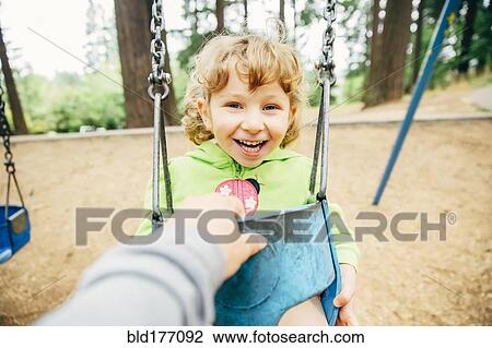 Stock Image - Caucasian mother pushing daughter on swing. Fotosearch