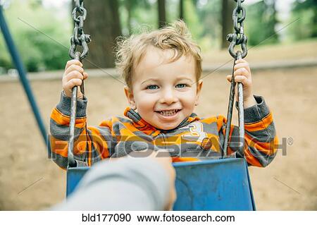 Stock Image - Caucasian mother pushing son on swing. Fotosearch