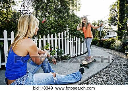 Stock Photo - Caucasian mother watching daughter ride skateboard. Fotosearch