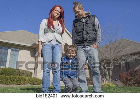 Stock Image - Caucasian parents and son smiling in yard. Fotosearch