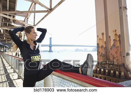 Stock Image - "Caucasian runner stretching on waterfront, New York, New York, United States". Fotosearch