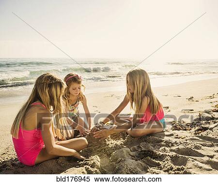 Stock Photography - Caucasian sisters building sandcastle on beach. Fotosearch