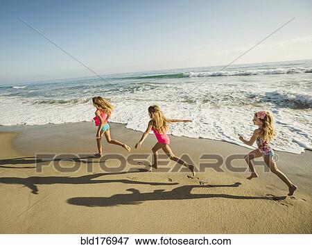 Stock Photo - Caucasian sisters running on beach. Fotosearch
