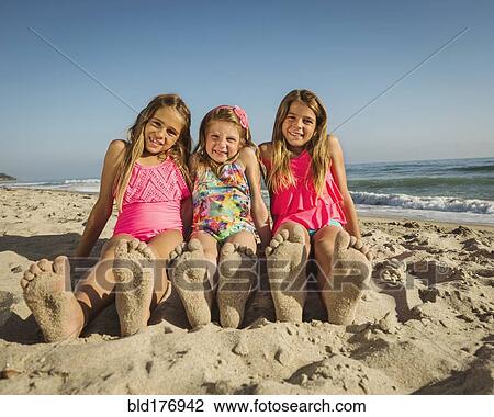 Stock Image - Caucasian sisters with sandy feet on beach. Fotosearch