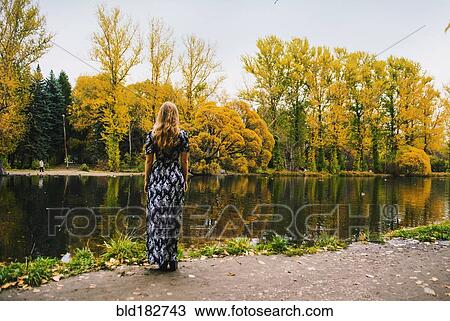 Stock Image - Caucasian woman admiring pond in park. Fotosearch