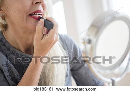Stock Image - Caucasian woman applying makeup in mirror. Fotosearch