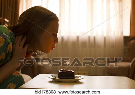 Stock Photo - Caucasian woman blowing birthday candle on cupcake. Fotosearch