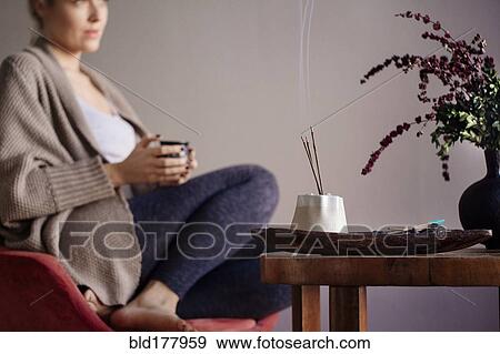 Stock Photo - Caucasian woman burning incense in living room. Fotosearch
