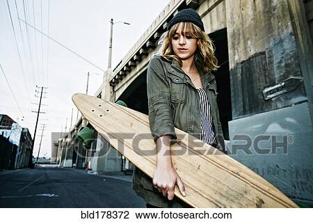 Stock Image - Caucasian woman carrying skateboard outdoors. Fotosearch
