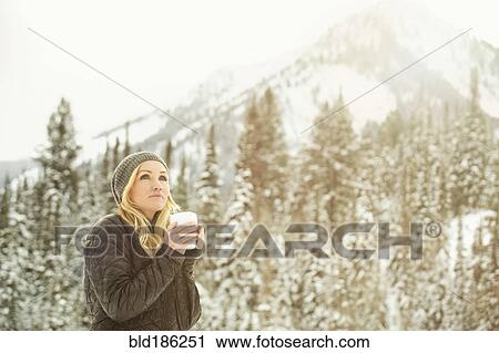 Stock Image - Caucasian woman drinking coffee in snow. Fotosearch