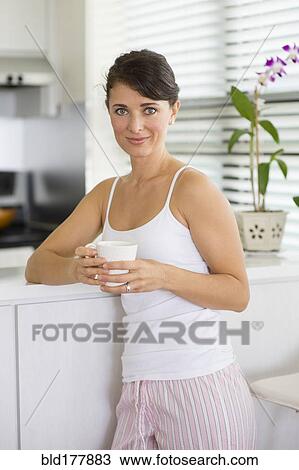Stock Image - Caucasian woman drinking coffee in kitchen. Fotosearch