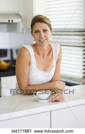 Stock Photo - Caucasian woman drinking coffee in kitchen. Fotosearch