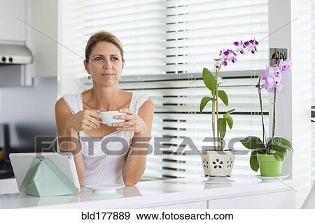 Caucasian woman drinking coffee in kitchen View Large Photo Image Stock Photo - Caucasian woman drinking coffee in kitchen. Fotosearch