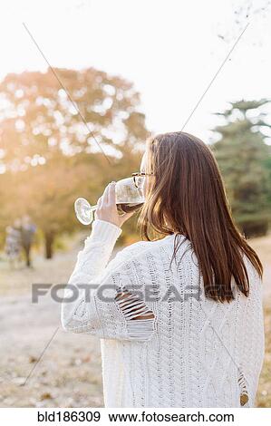 Stock Photo - Caucasian woman drinking wine in rural field. Fotosearch