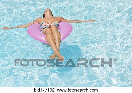 Stock Image - Caucasian woman floating in swimming pool. Fotosearch