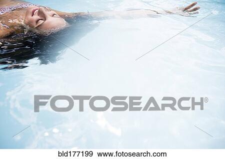 Stock Photo - Caucasian woman floating in swimming pool. Fotosearch