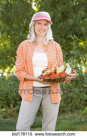 Stock Photography - Caucasian woman holding basket of vegetables in garden. Fotosearch