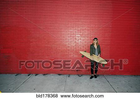 Stock Photo - Caucasian woman holding skateboard on sidewalk. Fotosearch