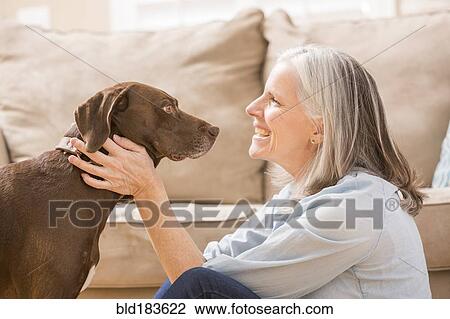 Stock Image - Caucasian woman hugging dog in living room. Fotosearch