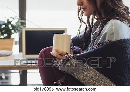 Stock Photography - Caucasian woman in blanket drinking cup of coffee. Fotosearch