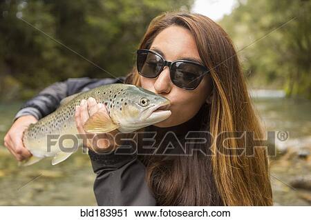 Stock Image - Caucasian woman kissing fish in remote river. Fotosearch