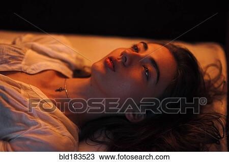 Stock Image - Caucasian woman laying on bed. Fotosearch
