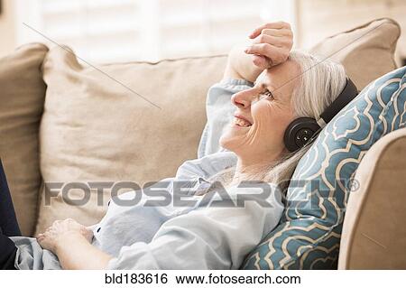 Caucasian woman listening to headphones on sofa View Large Photo Image Stock Photograph - Caucasian woman listening to headphones on sofa. Fotosearch
